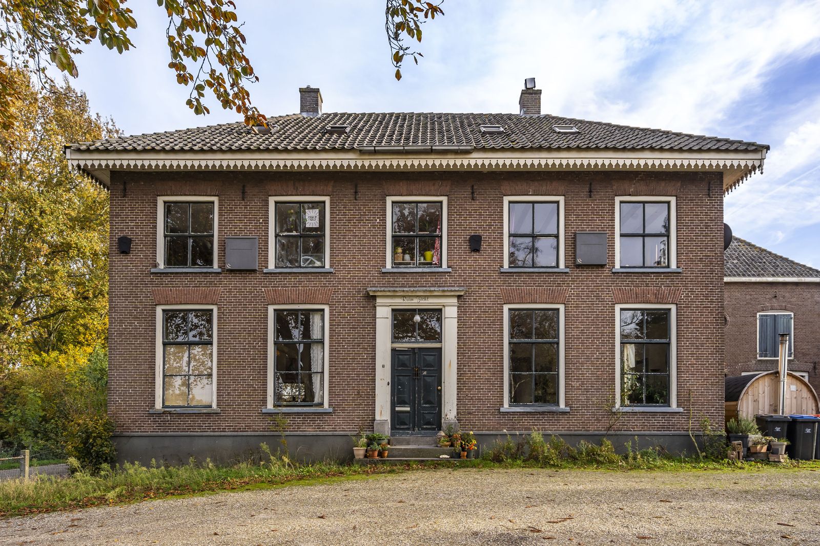 bakstenen woonhuis met een zadeldak en witte kozijnen langs een weg in Asch