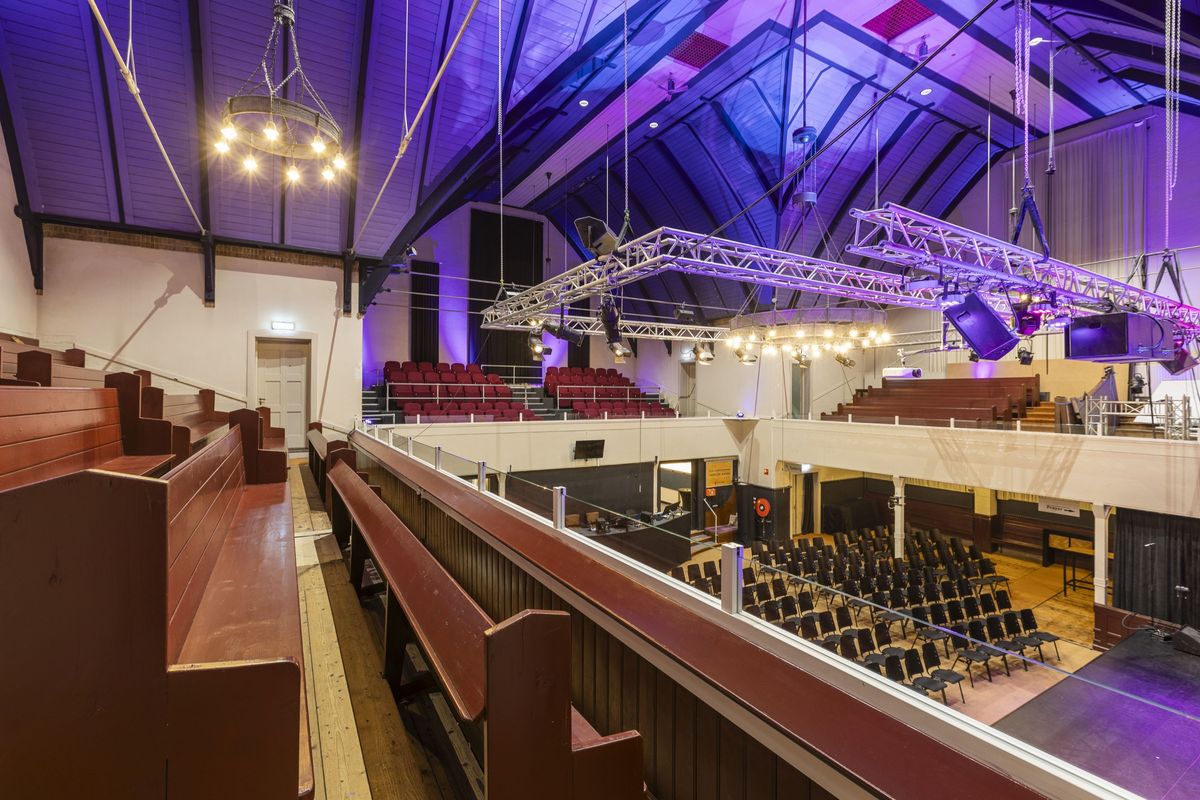 kerkzaal met galerij, houten banken en podiumverlichting in Assen