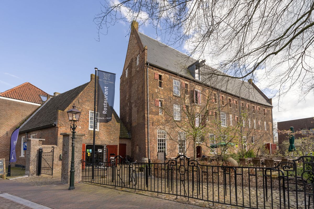 het Arsenaal in Doesburg achter een smeedijzeren hek, een hoog bakstenen gebouw onder een pannendak