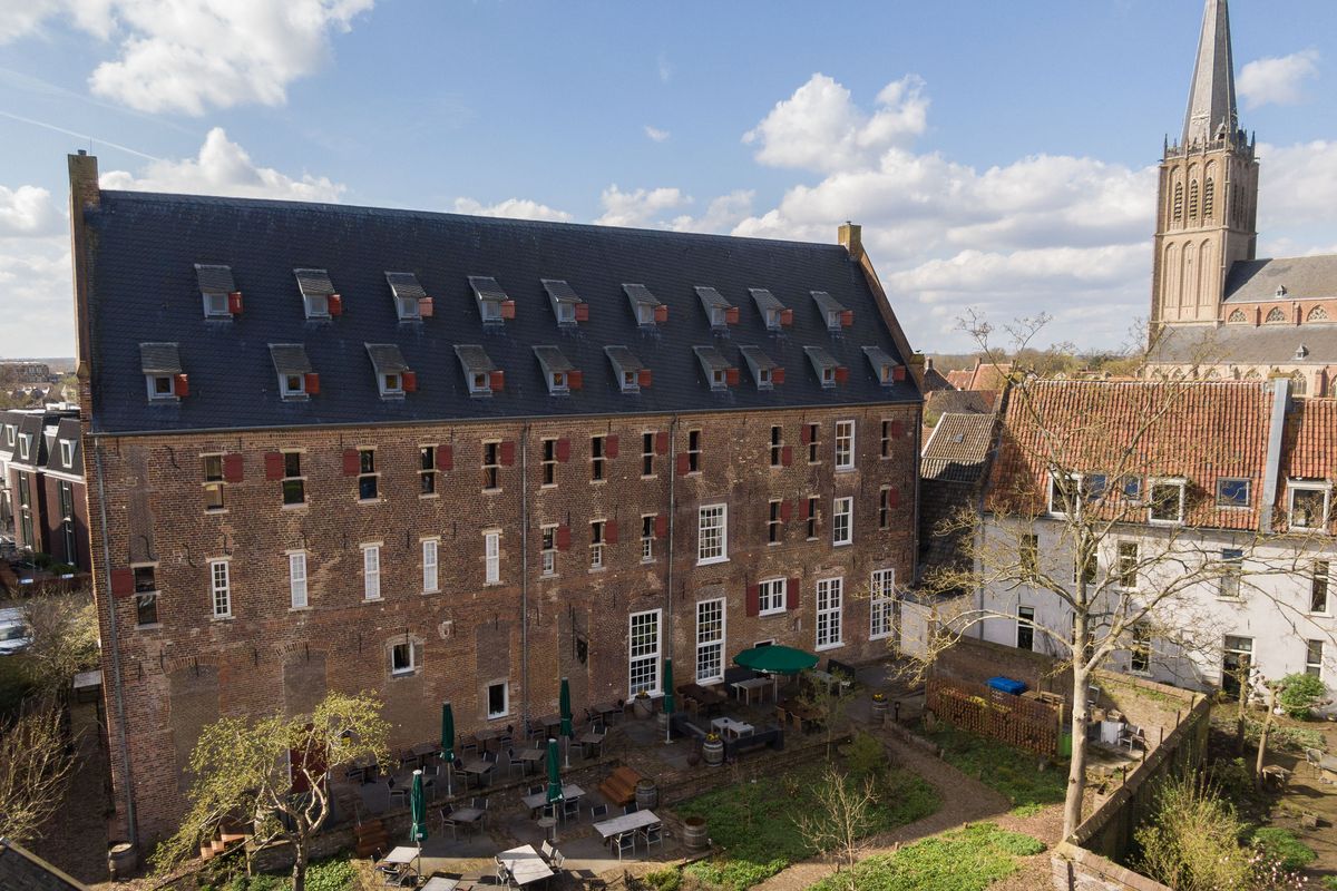 het Arsenaal in Doesburg, een groot bakstenen gebouw met een donker dak vol dakkapellen, naast de toren van de kerk