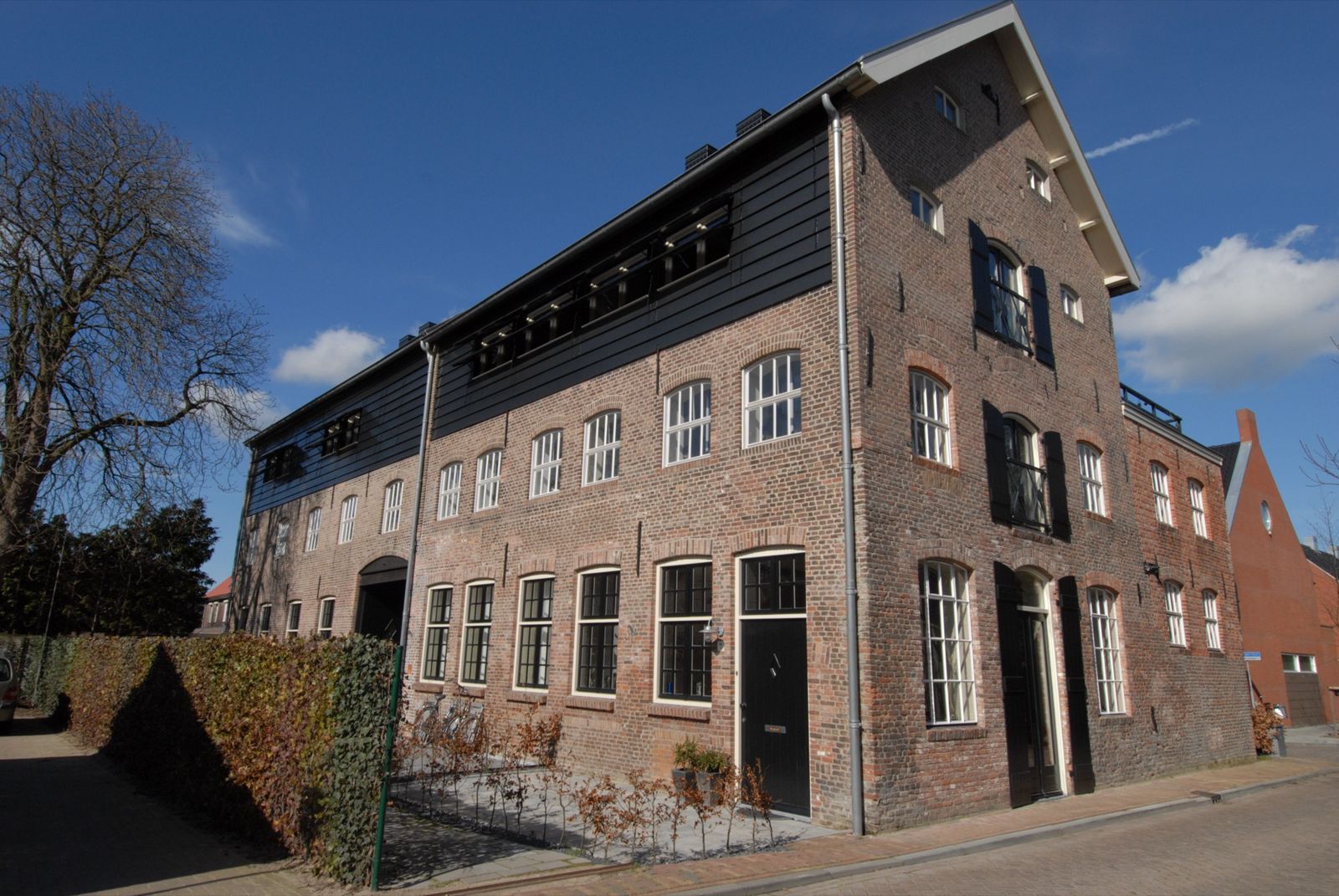 voormalige leerlooierij in Dongen met een bakstenen gevel, een zwarte houten beschieting en hoge ramen onder een blauwe lucht