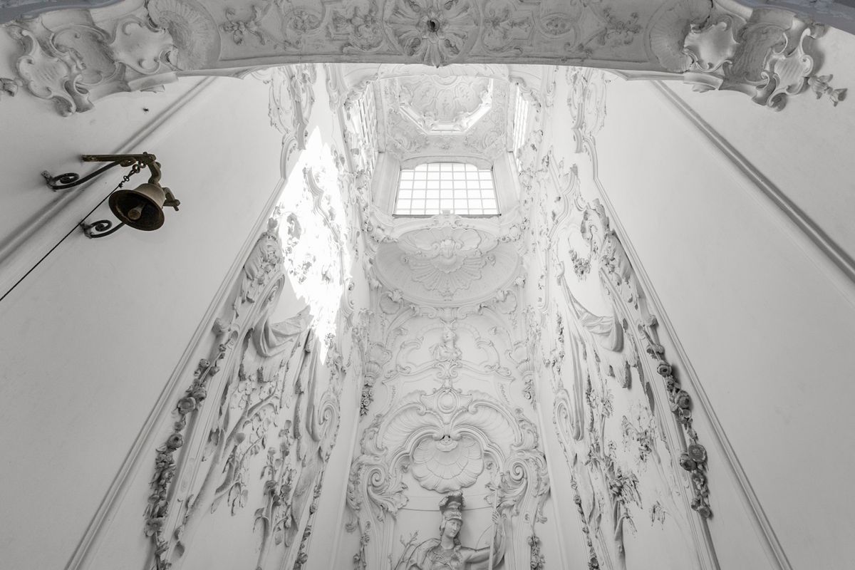 wit stucwerk met ornamenten op de wanden en het plafond van een trappenhuis, van onderaf gezien