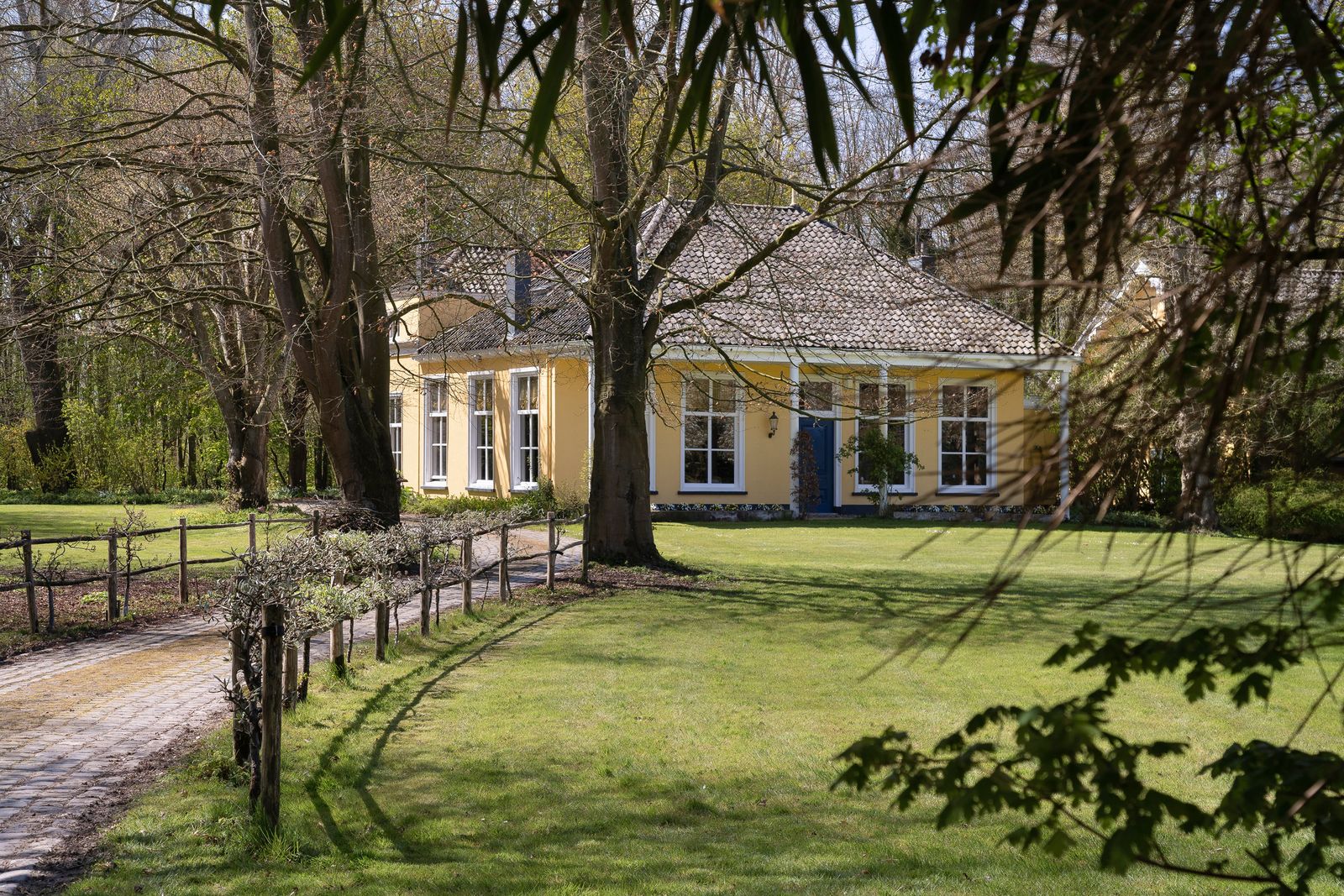 geel landhuis met een pannendak aan een pad tussen bomen en gazon in Noordgouwe