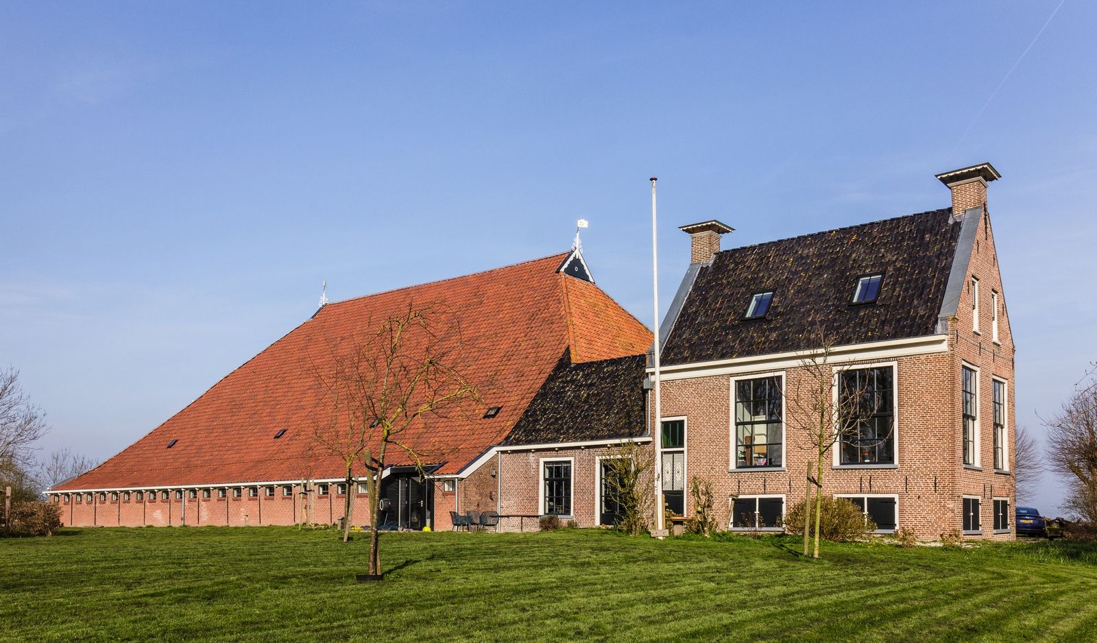 kop-hals-rompboerderij in Reduzum: een lange rode dakkap naast een bakstenen voorhuis, voor een grasveld