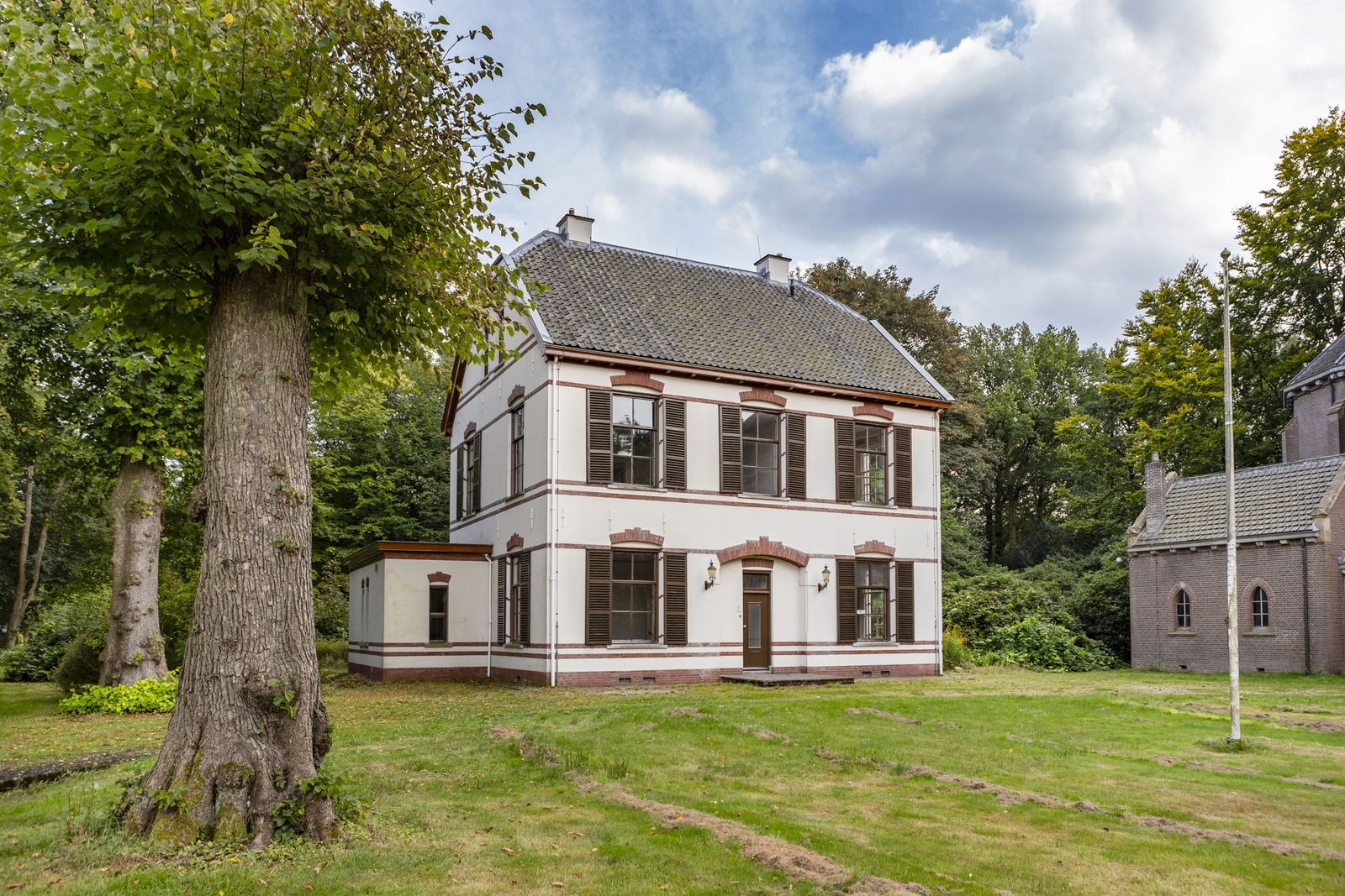 witte villa met een grijs schilddak en een grote boom ervoor in Veenhuizen