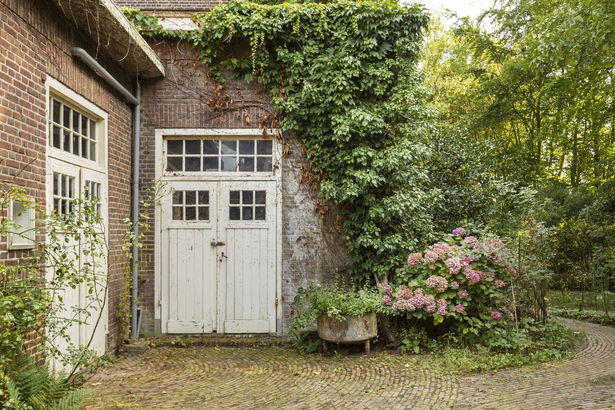 witte houten deuren in een bakstenen muur met klimop in Vlijmen