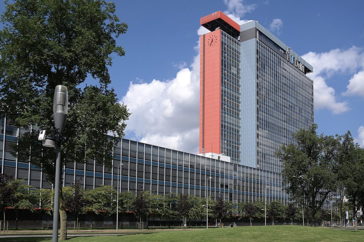 hoge kantoortoren met een rode kop naast een lage glazen vleugel op de campus in Delft