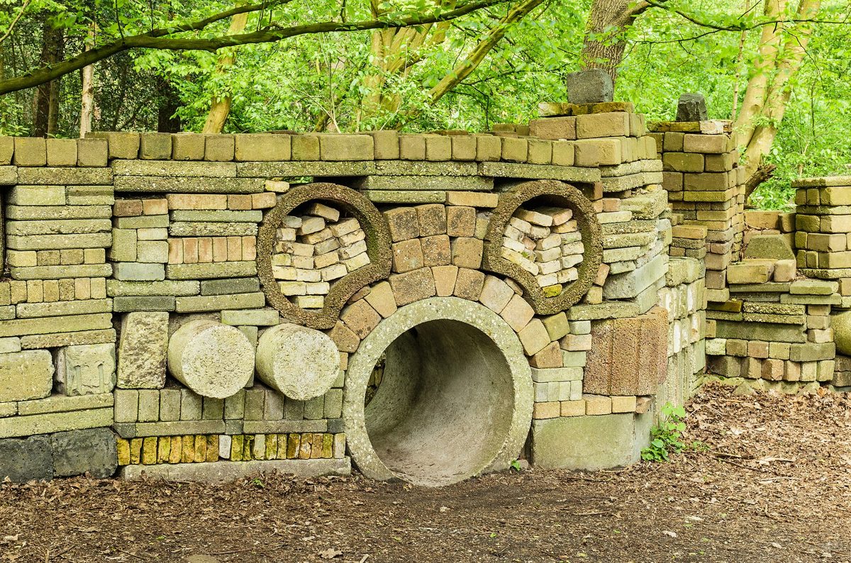 gestapelde bakstenen en betonbuizen in een muur van de Ecokathedraal tussen de bomen